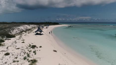 Aerial-view-dolly-out-coastline-cayo-de-agua-island-with-beach-umbrellas-and-people-joy-beach-day