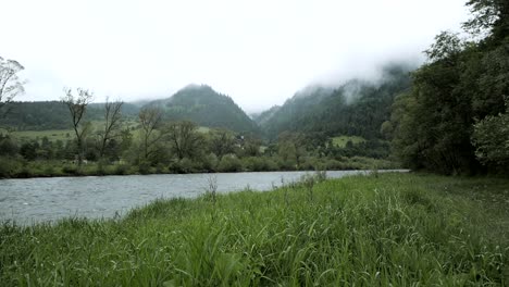 Time-lapse-of-a-small-river-in-nature,-hills-in-the-fog-are-visible-in-background
