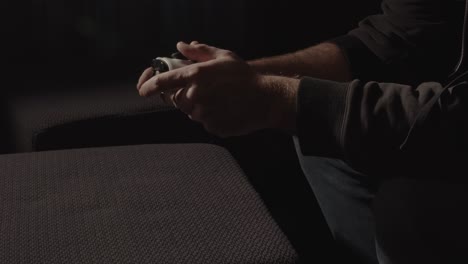 Male-hands-playing-with-videogame-controller-while-light-emitted-from-the-television-is-flashing
