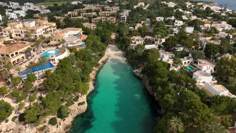 Aerial-view-of-drone-flying-close-to-a-small-beach-in-Cala-d'Or,-Mallorca-with-crystal-clear-waters