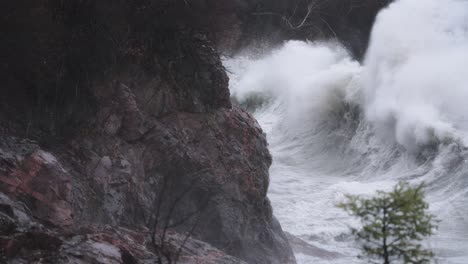 Huge-stormy-waves-crash-against-granite-coastal-cliffs-on-a-gloomy-day-in-slow-motion