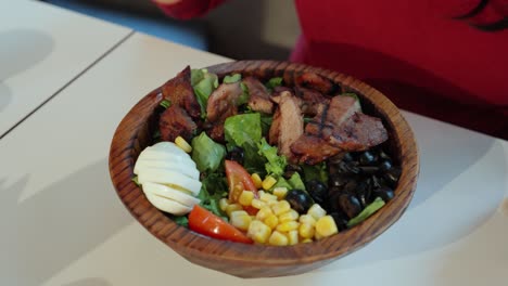 Close-up-of-woman's-grilled-pork-salad-in-wooden-bowl-as-she-begins-eating