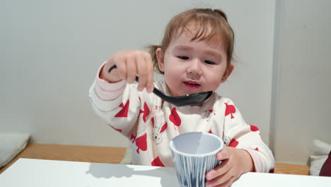 Young-Asian-toddler-drinks-water-from-mug-using-chirirenge,-Japanese-soup-spoon