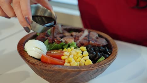Woman-pouring-oriental-sauce-over-grilled-pork-salad-in-wooden-bowl