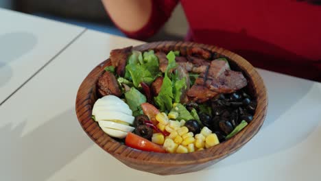 Top-down-view-of-woman-eating-grilled-pork-salad-from-wooden-bowl