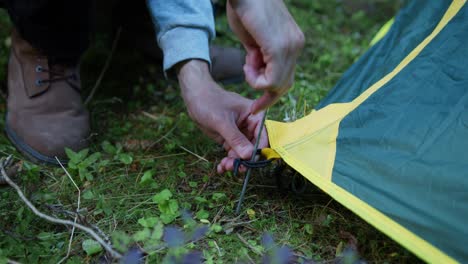 Close-up-shot-of-man-setting-up-a-tent-by-putting-a-herring-in-the-ground-while-camping-in-the-woods