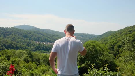 Man-in-white-t-shirt-is-looking-over-the-jungle-from-a-viewpoint-while-drinking-coffee