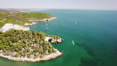 Drone-flying-upwards-and-in-circulair-motion-over-the-coastline-of-Gargano-national-park-showing-an-arch-in-the-sea-and-boats-passing-by-in-4k