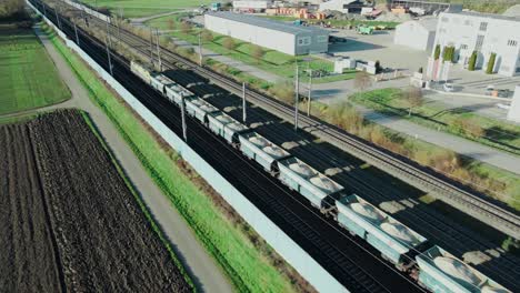 A-freight-train-carrying-gravel-through-an-industrial-area-is-followed-by-a-drone-flying-next-to-the-train-tracks