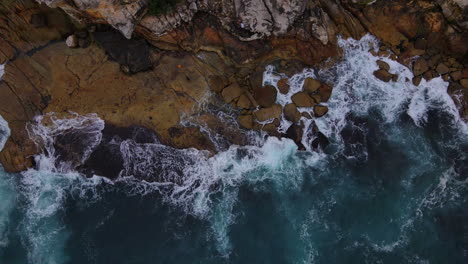 Top-view-of-blue-green-ocean-waves-smashing-against-rocky-coastline-in-Australia