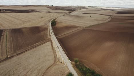 Drone-flying-in-circulair-motion-around-an-old-bridge-with-train-tracks-laying-between-farmfields-in-Italy-in-4k