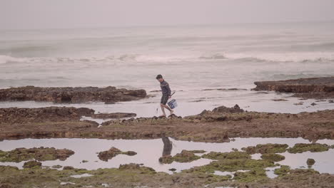 Tight-close-up-shot-of-young-fisherman-walking-on-rocky-shore-of-Atlantic-Ocean-in-Essaouira-Morocco