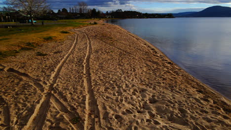 Empty-sand-beach-with-tire-tracks-and-gentle-waves-on-shore-in-New-Zealand