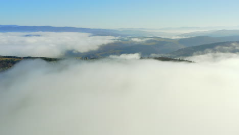 Aerial-establishing-shot-over-foggy-mountain-peak,-small-clearing-in-forest