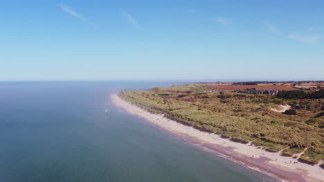 Aerial-shot-from-high-above,-rising-over-a-British-beach-on-a-scorching-summer-day-while-families-play-below