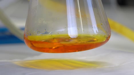 Close-up-of-orange-liquid-dripping-into-a-chemistry-flask