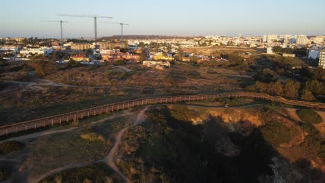 Aerial-view,-drone-shots-4k,-revealing-Praia-de-Dona-Ana,-Lagos,-with-man-cycling-at-sunrise,-Algarve,-Portugal