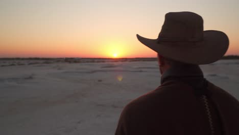 close-up-of-a-man-dressed-as-a-cowboy-standing-on-a-salt-field-watching-the-sunrise