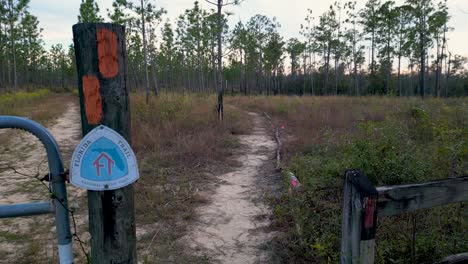Florida-trail-sign-on-fencepost-at-trailhead-near-econfina-creek-with-hiking-trail-in-background