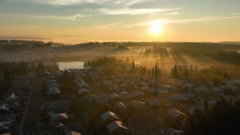 Aerial-view-of-the-sun-rising-over-a-frosted-neighborhood-with-morning-fog
