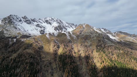 Impresionantes-Imágenes-De-Drones-De-Un-Valle-Alpino-En-Otoño-Con-árboles-De-Diferentes-Colores-Y-Un-Río-Que-Fluye-En-El-Suelo-Del-Valle-Rodeado-De-Picos-Montañosos-Nevados