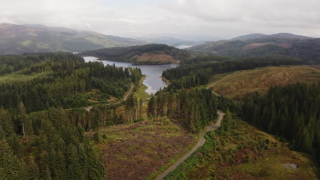 A-sweeping-aerial-shot-rises-to-reveal-a-calm-Scottish-loch-nestled-in-a-huge-lush-forest