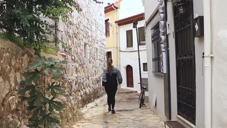 Mujer-Caminando-Por-Un-Callejón-En-Un-Pueblo-Blanco-De-Santorini,-Grecia