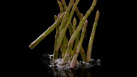 Bunch-of-asparagus-fall-into-water-isolated-on-black-background,-ultra-slow-motion