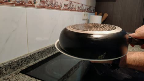 the-hands-of-the-cook-using-a-plate-to-turn-the-Spanish-potato-and-egg-omelette-in-the-pan-and-finish-cooking-in-electric-hob-cooker,-Shot-blocked-close-up,-Galicia,-Spain