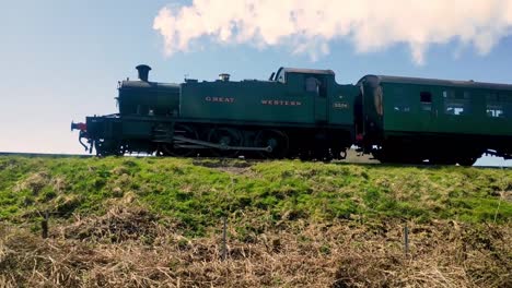 Steam-train,-in-the-country-side,-the-remains-of-the-Royal-Corfe-castle-in-background,-slow-pan-following-subject
