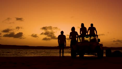 Silhouette-showing-group-of-people-with-quad-watching-sunset-and-jumping-kiteboarder-in-ocean---static-wide-shot