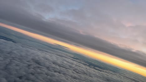 Pilot-point-of-view-from-a-jet-cockpit-during-a-left-turn-at-dawn-while-flying-between-layers-of-clouds-with-an-ogange-sky