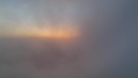Flying-through-clouds-revealing-sunrise-over-green-valley