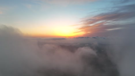 Flying-towards-sunrise-over-green-valley-with-clouds