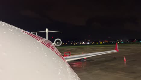 Night-view-of-the-upper-part-of-the-fuselage-of-a-jet-in-a-rainy-and-cold-night-with-other-traffics-in-the-airport