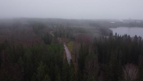 Image-of-drone-descending-from-high-up-and-appearing-from-fog-while-uncovering-a-huge-lake,-forest-and-a-factory-in-a-distance