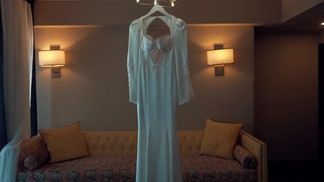 A-forward-smooth-shot-of-a-bridal-wedding-dress,-hanging-in-a-decorate-room