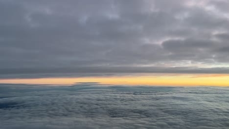Pilot-view-from-a-jet-cockpit-while-flying-between-layers-of-clouds-at-dawn-with-an-orange-sky,-at-10000m-high-in-a-cold-winter-moorning