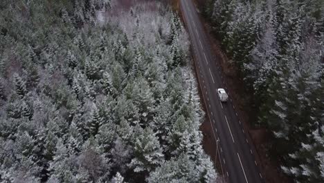 slow-moving-drone-shot-of-a-car-driving-up-a-road-and-driving-through-frosty-forest-and-paved-road