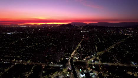 Santiago-de-Chile-Sunset,-Atenas-Roundabout,-Urban-Traffic-Aerial-Sky-City-Roads-Gradient-Horizon-Golden-and-Yellow-over-Andean-Cordillera