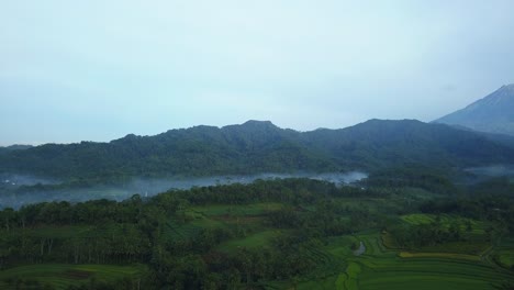 Clouds-flying-between-rural-mountains-covered-with-green-plants-and-leaves-during-cloudy-day-in-Asia---Aerial-view