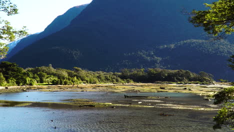 Silhouette-of-people-enjoys-shallow-river-in-Milford-Sound,-zoom-out-view