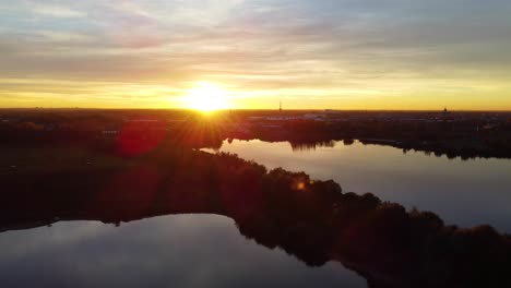 Reflective-lake-water-during-golden-sunset-in-Belgium,-aerial-drone-view