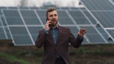 A-solid-man-in-business-clothes-is-talking-on-the-phone-against-the-background-of-solar-panels
