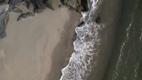 A-top-down-view-over-an-empty-beach-as-the-waves-gently-crash-onto-the-shore-in-slow-motion