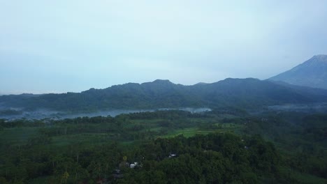 Reveal-drone-shot-of-rural-landscape-of-plantation-with-forest-and-hill-in-the-misty-morning---Tropical-landscape-of-Indonesia