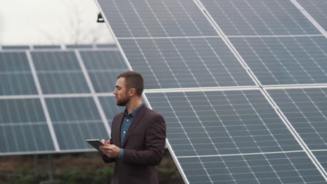 A-businessman-in-a-jacket-with-a-tablet-inspects-a-solar-power-plant