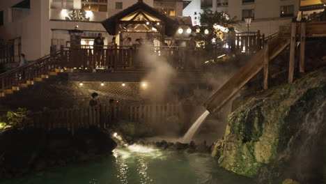 Tourists-gathering-and-taking-photographs-of-the-symbolic-hot-water-field-of-Kusatsu-Onsen-in-Gunma-in-the-evening-after-light-up-with-steaming-hot-water-coming-out