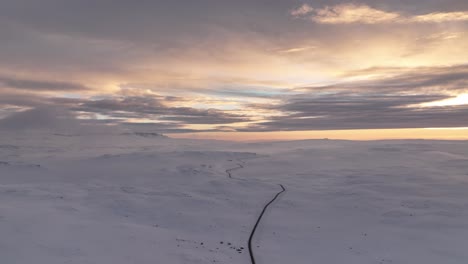 Sunset-shot-of-a-long-arctic-mountain-road-with-snow-covered-mountains