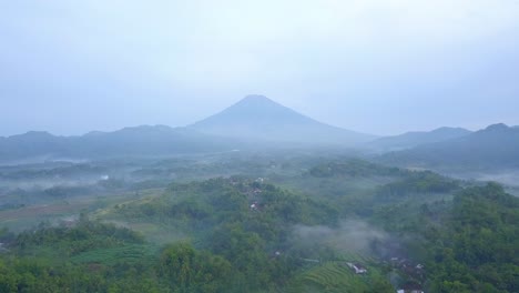 Aerial-view-of-rural-landscape-in-the-misty-morning-with-huge-mountain-on-the-background